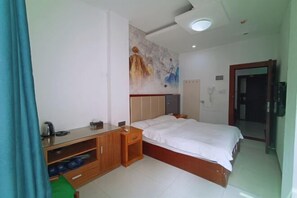 A hotel room with a bed, a wooden nightstand, a desk with a chair, a wall-mounted TV, and a painting. - Fogang Xingshu Fashion Hotel (Fogang)