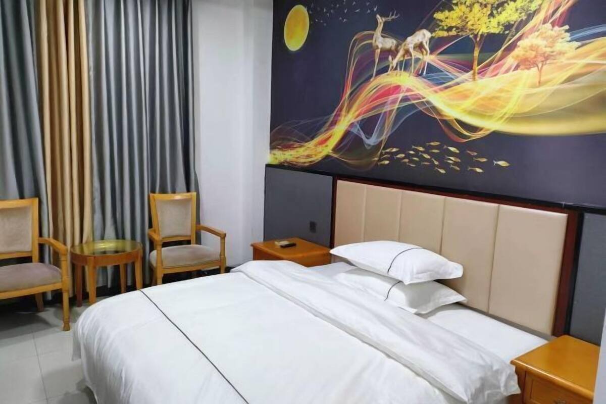 A hotel room with a bed, two chairs, a small table, and a nightstand.