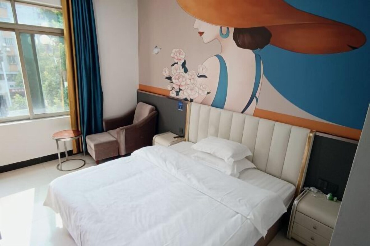 A hotel room with a large bed, a sofa, a nightstand, and a wall mural.