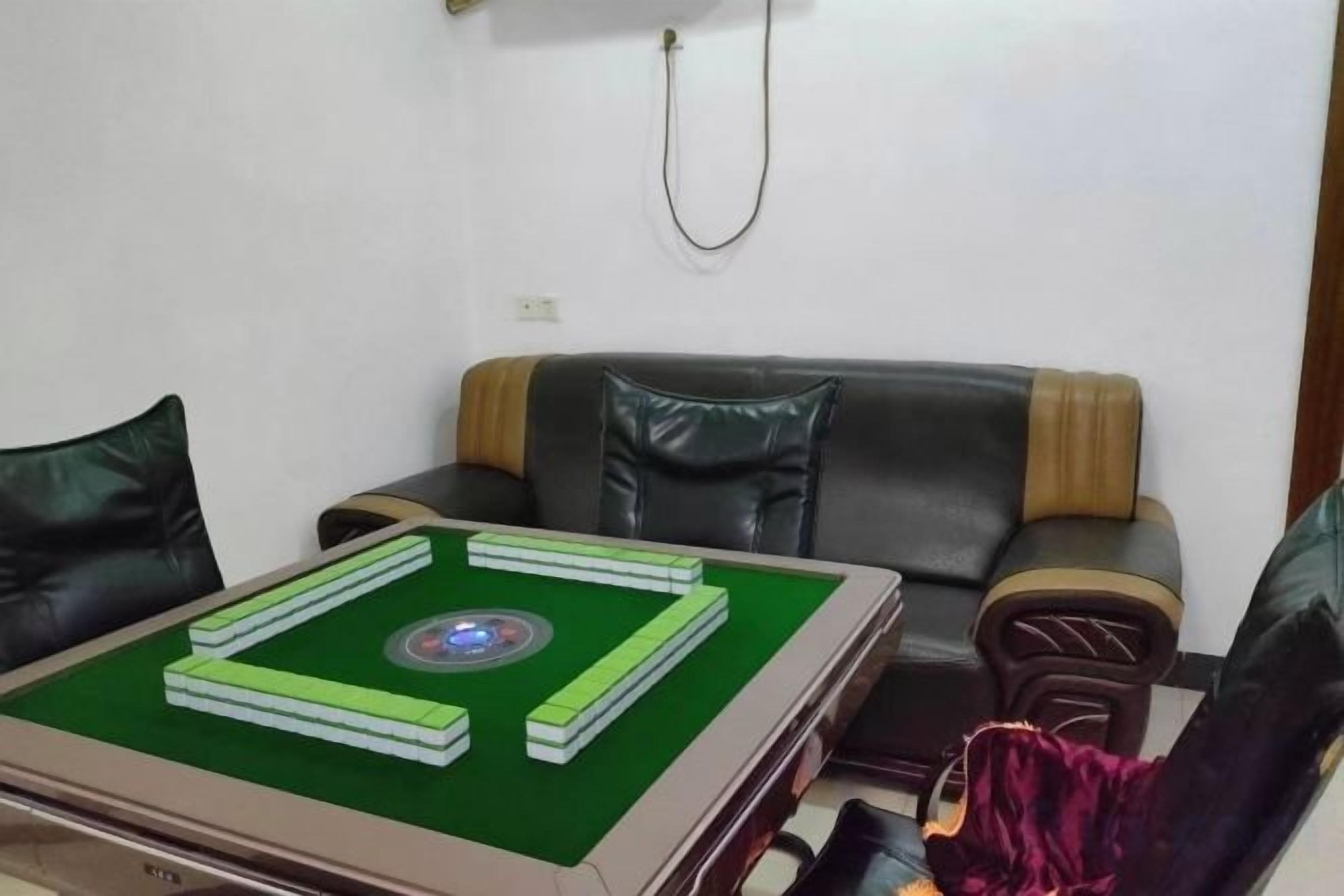A room with a green felt game table, a black leather sofa, and a red chair.