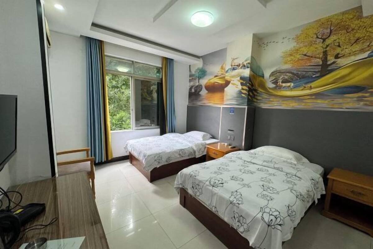 A hotel room with two beds, a TV, a desk, and a window with curtains.