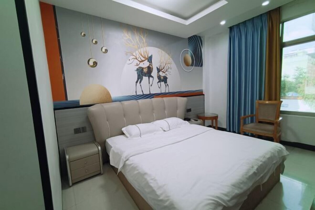 A bedroom with a large bed, a bedside table, a chair, and a wall mural.