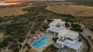 Eine moderne weiße Villa mit Pool, eingebettet in eine natürliche Landschaft mit Blick auf den Sonnenuntergang.