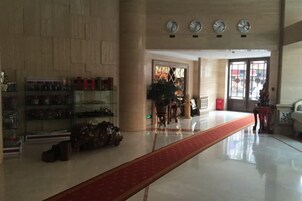Un vestíbulo de hotel con alfombra roja, un mostrador de recepción y un amplio ventanal con vistas.