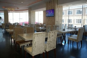 A spacious restaurant with high ceilings, large windows, and a flat-screen TV mounted on the wall.