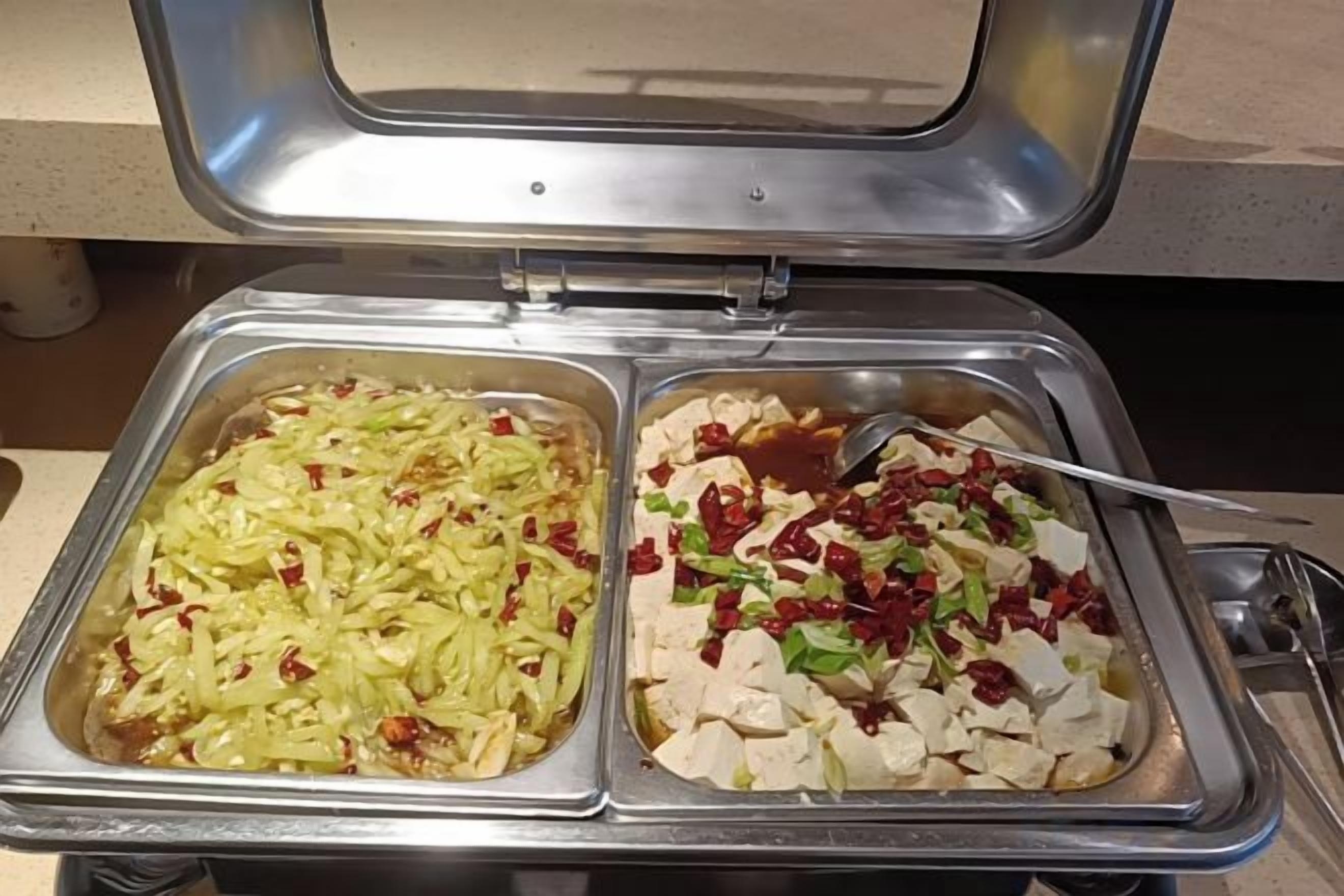 A buffet with two metal trays, one containing shredded vegetables and the other with mixed meats and greens.