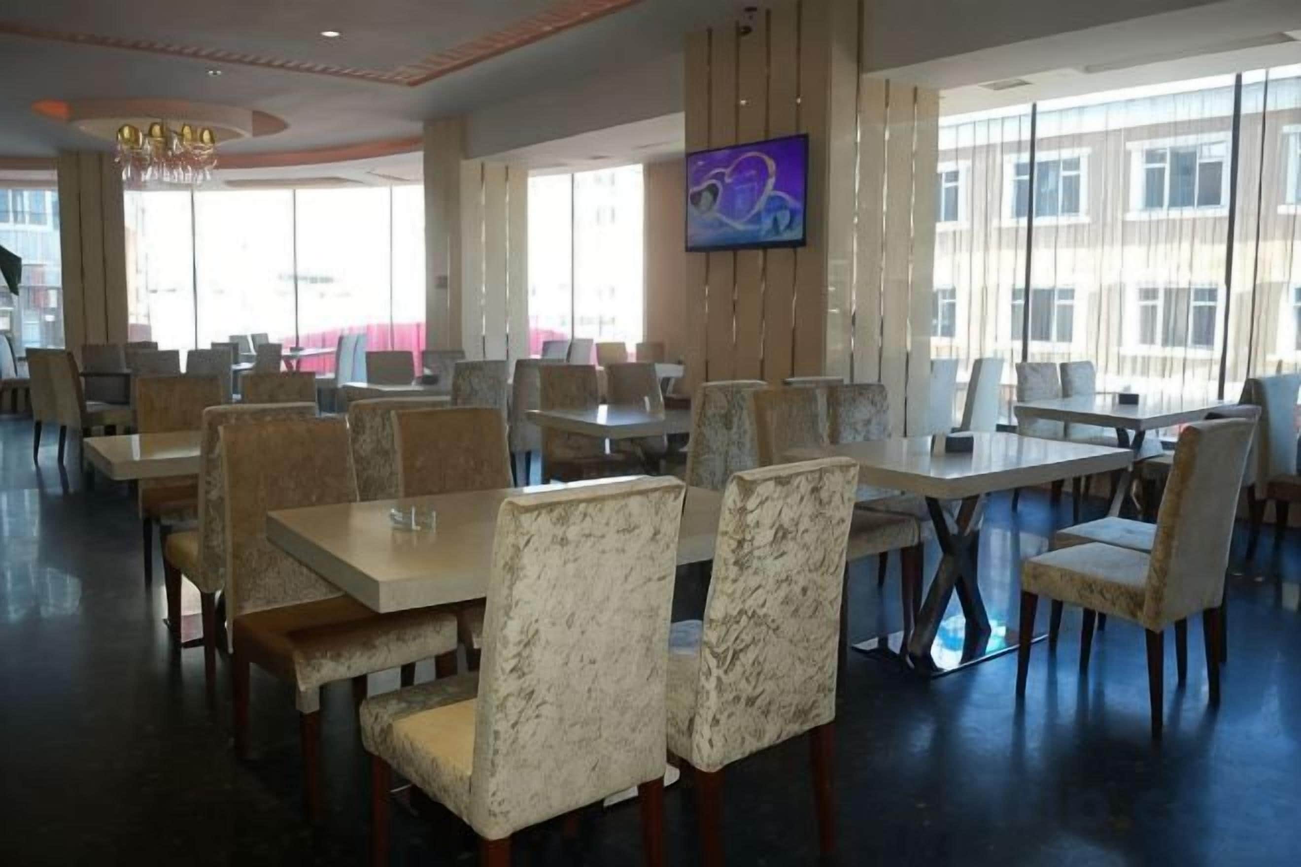 A spacious dining area with multiple tables and chairs, large windows, and a flat-screen TV mounted on the wall.