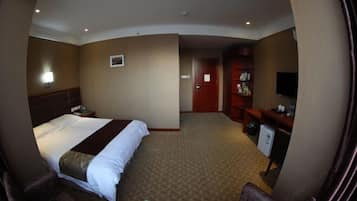 A hotel room with a large bed, a desk, a television, and a small kitchenette.