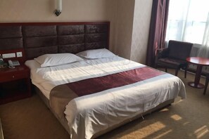 Een hotelkamer met een groot bed, een nachtkastje met telefoon, een stoel en een kleine tafel.