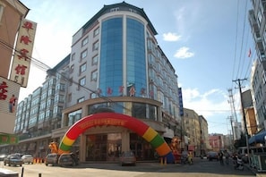 A multi-story hotel with a curved facade, a prominent entrance with a colorful arch, and a clear sky above.