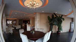 A dining area with a round table, chairs, a chandelier, and potted plants.