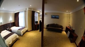 A hotel room with two beds, a sofa, a desk with a computer, and a TV.