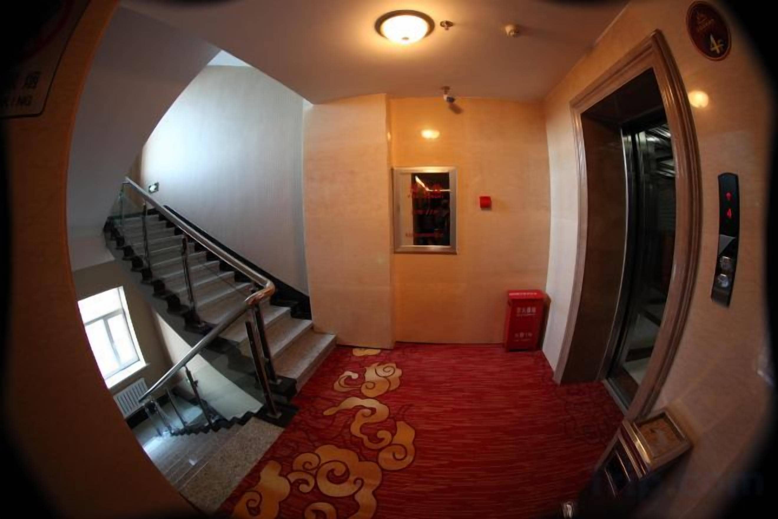 Un couloir d’hôtel avec un tapis rouge, un escalier et un ascenseur.