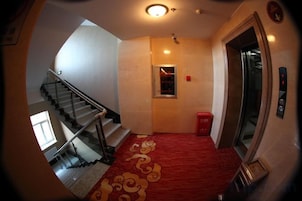 Un pasillo de hotel con alfombra roja, una escalera y un ascensor.