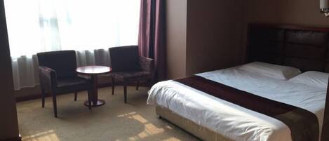 Een hotelkamer met een bed, een ronde tafel, twee stoelen en een raam met gordijnen.