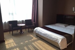 Een hotelkamer met een bed, een ronde tafel, twee stoelen en een raam met gordijnen.