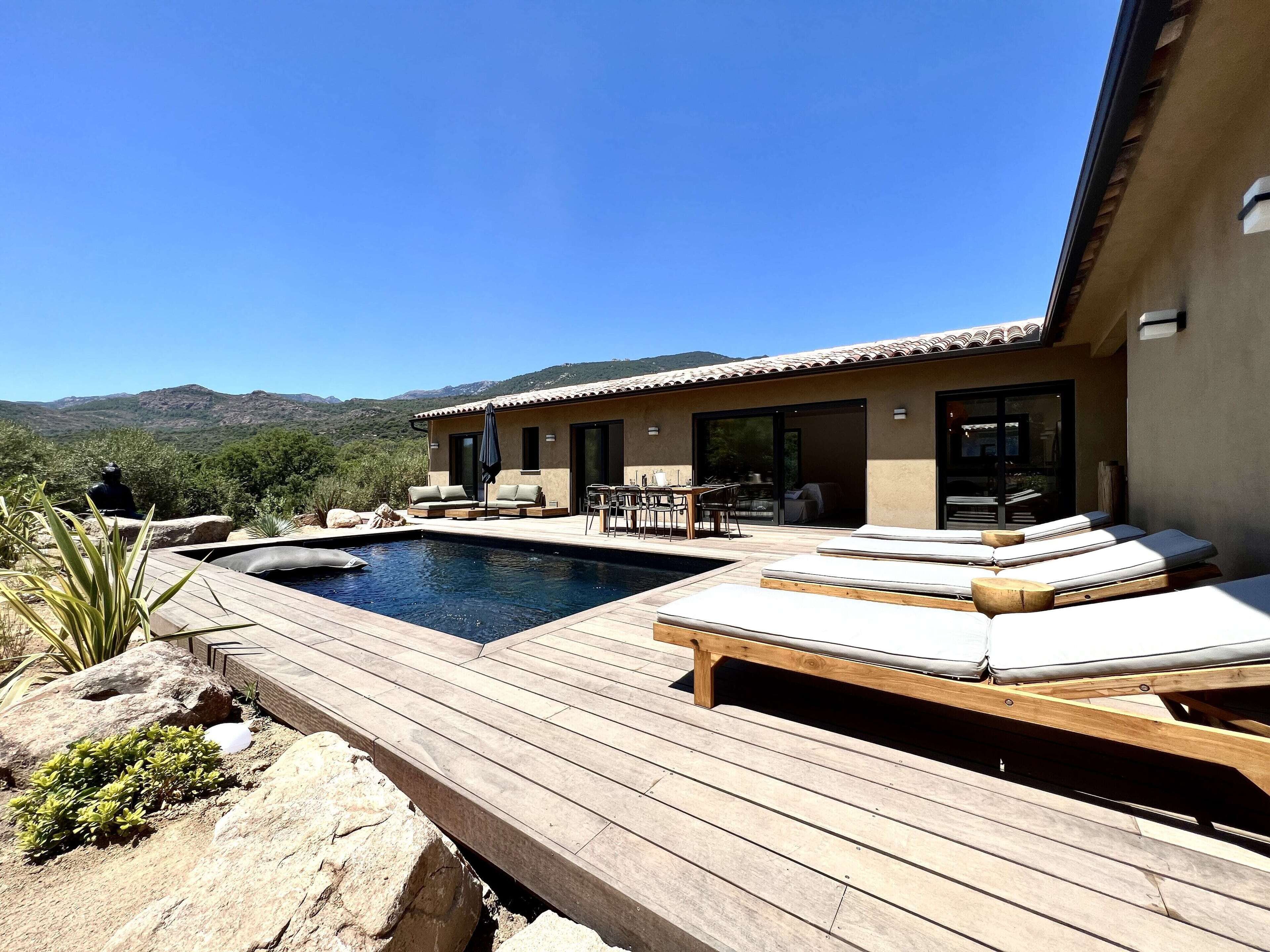 A poolside area with lounge chairs, a dining set, and a view of mountains.