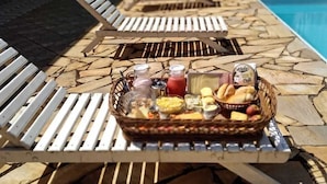 Un espace aménagé au bord de la piscine, avec des chaises longues et une table sur laquelle se trouve un panier rempli de collations et de boissons.