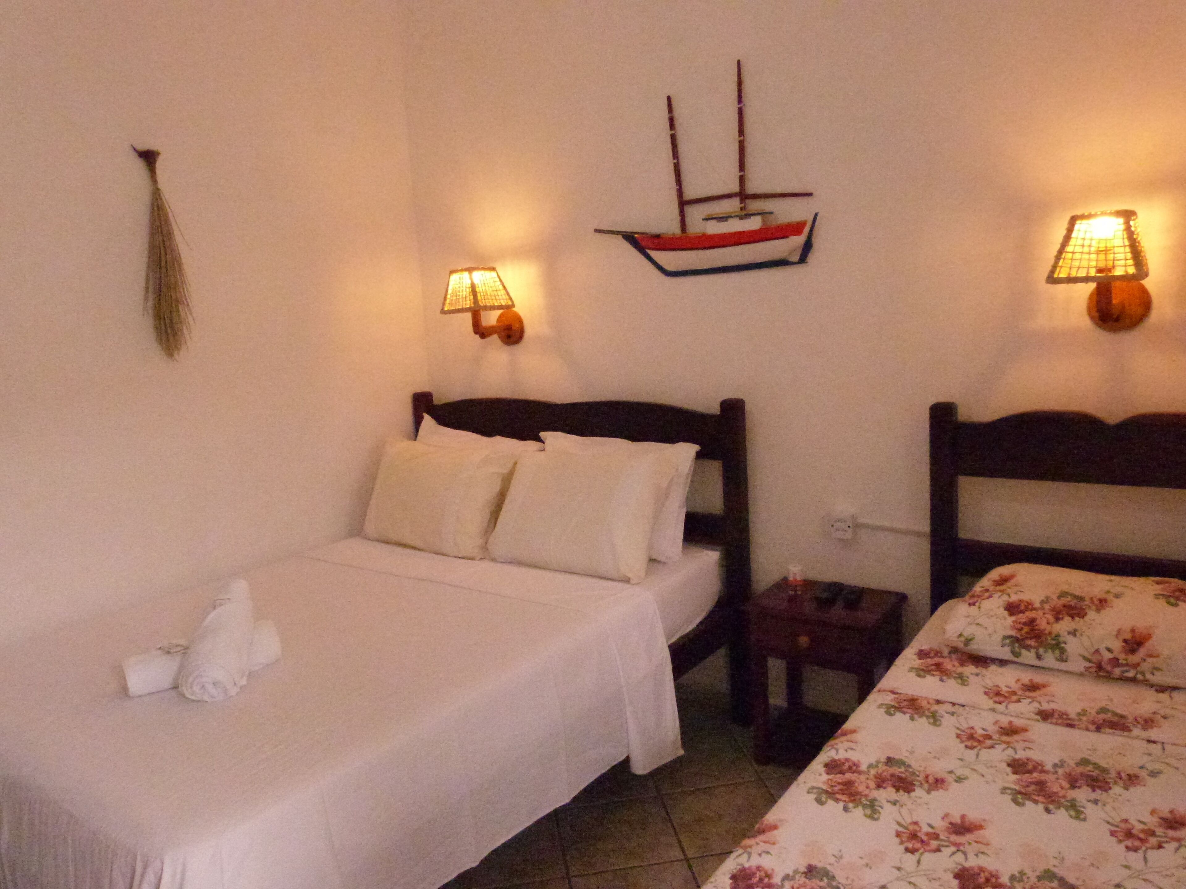 A room with a bed, a smaller bed, a nightstand, a lamp, and a wall-mounted ship decoration.