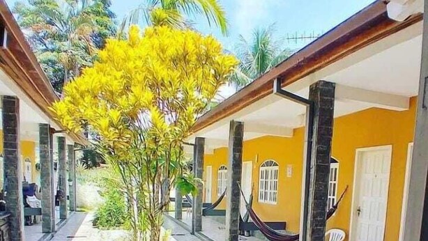 Un espace extérieur abrité, doté d’un arbre central, d’un sol carrelé et d’un bâtiment jaune avec des fenêtres et des portes.