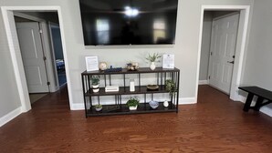Una sala de estar con un televisor de pantalla plana montado en la pared, una mesa consola de madera con objetos decorativos y un banco en una esquina.