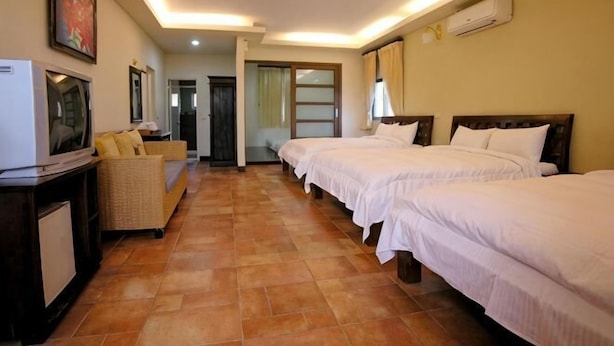 Una habitación de hotel con tres camas, televisión, sofá y una mesita.