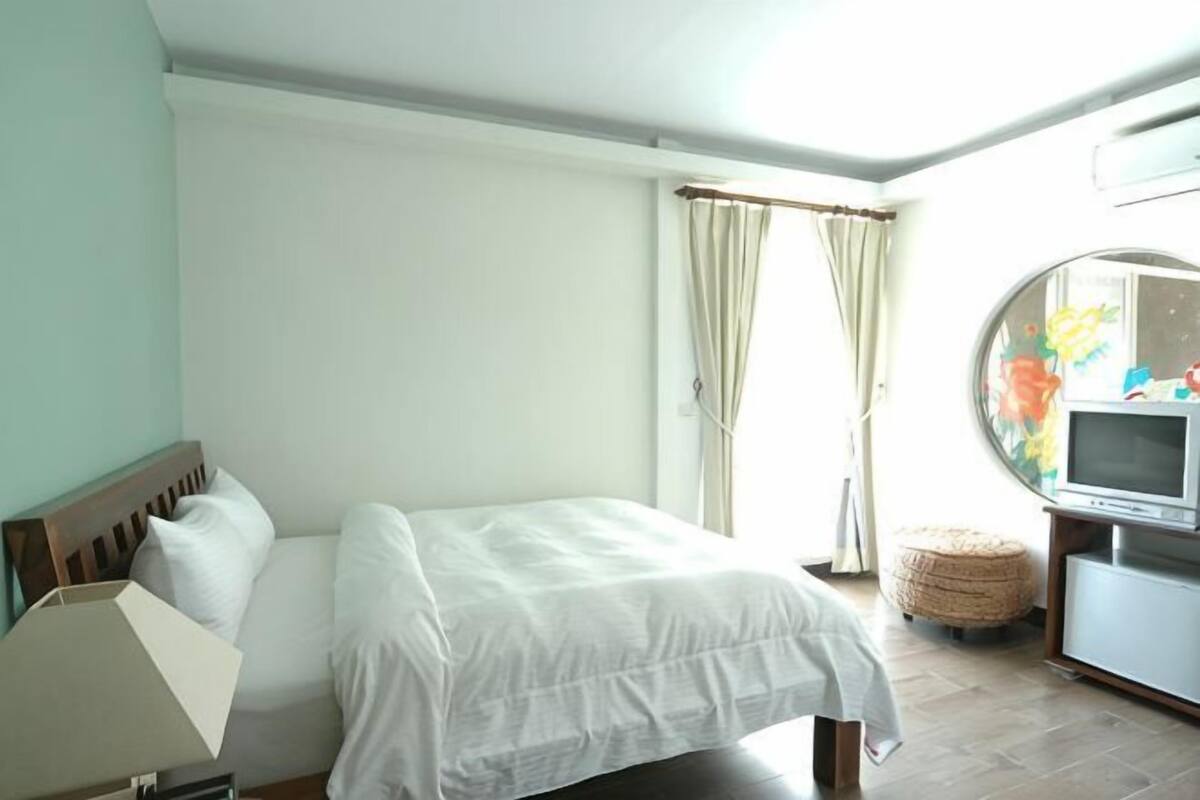A bedroom with a bed, a television, and a window with curtains.