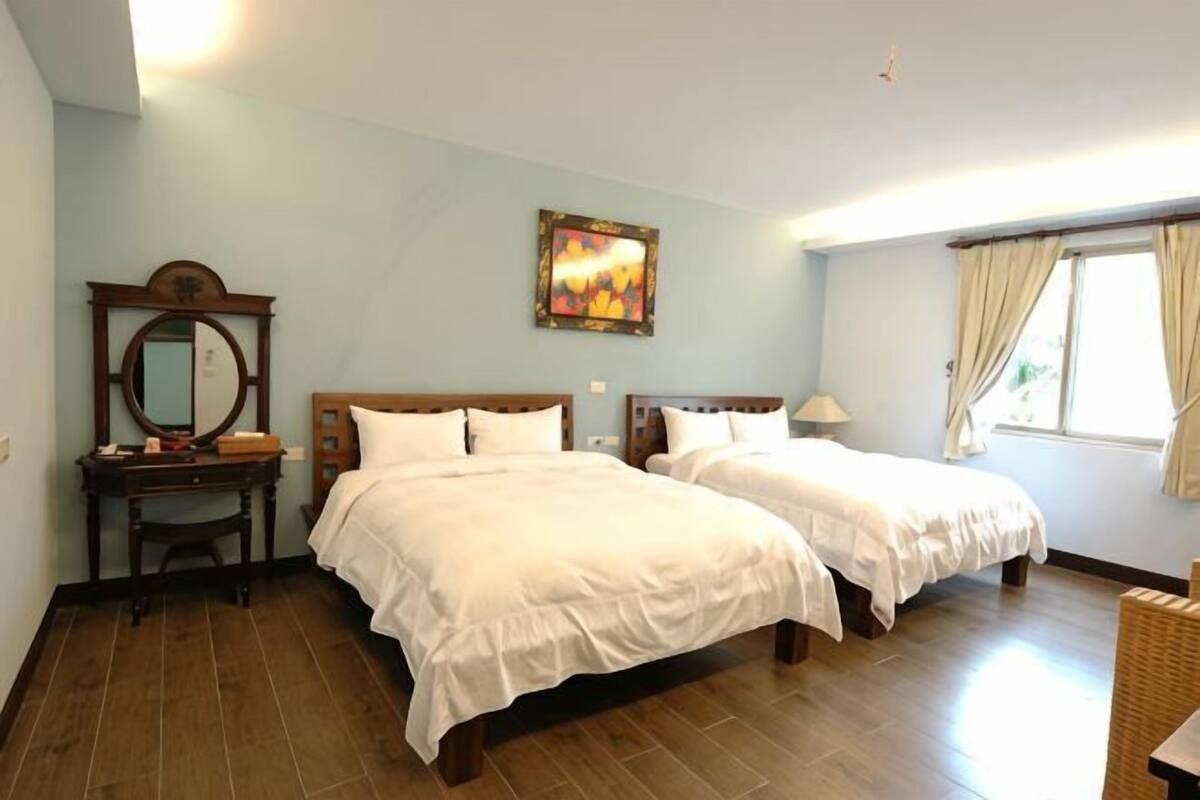 A room with two beds, a wooden dresser, a mirror, and a painting on the wall.