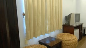 Una habitación con televisión sobre un pie de madera, una mesita pequeña y una cesta tejida.