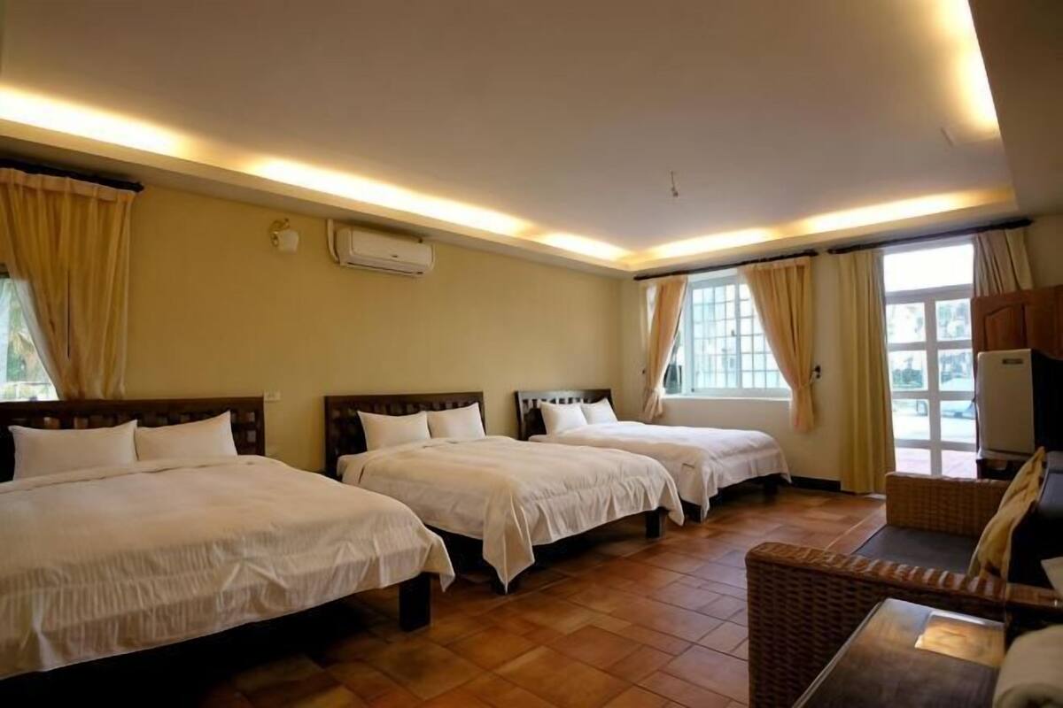 A hotel room with three beds, a sofa, and a large window.