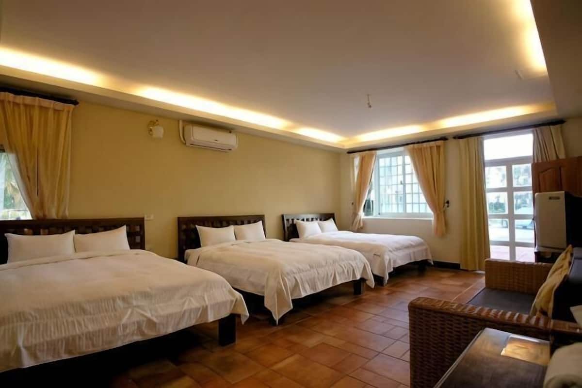 Quarto de hotel com três camas, um sofá e uma janela grande.