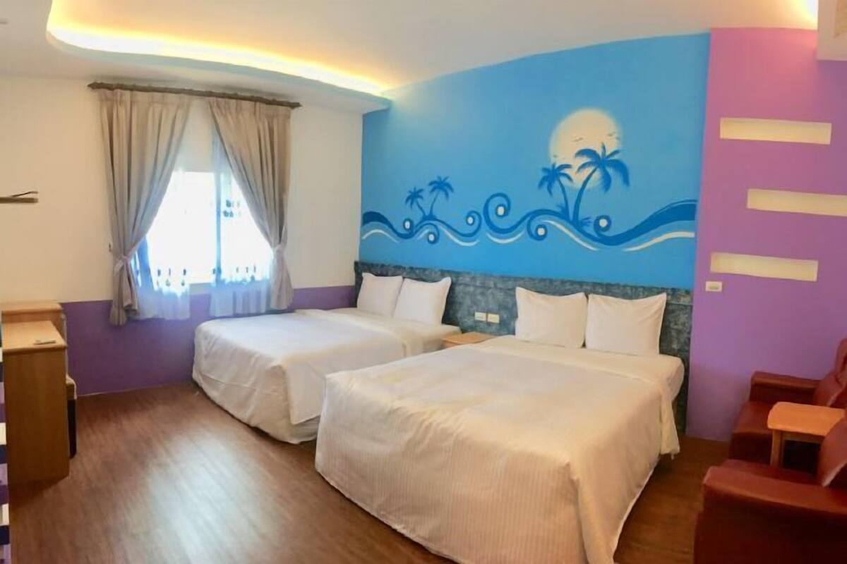 A hotel room with two beds, a window with curtains, a wall mural, and a wooden floor.