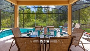 A covered outdoor area with a pool, seating, and a table set for dining. - Luxury 4BR Retreat w/ Pool, Game Room & Close to Disney Attractions (Davenport)