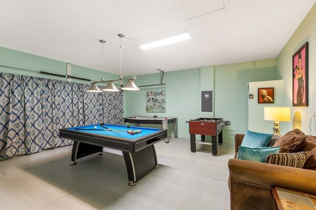 A room with a pool table, two foosball tables, a sofa, and a lamp.
