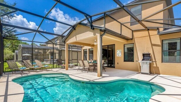 A swimming pool with lounge chairs, a covered patio, and a grill area. - Luxury 4BR Retreat w/ Pool, Game Room & Close to Disney Attractions (Davenport)
