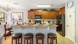 A kitchen with wooden cabinets, a central island with stools, a microwave, and a refrigerator. - Luxury 4BR Retreat w/ Pool, Game Room & Close to Disney Attractions (Davenport)