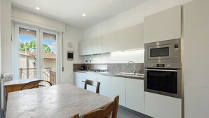 Una cocina moderna con armarios blancos, horno empotrado y comedor con mesa y sillas de madera.