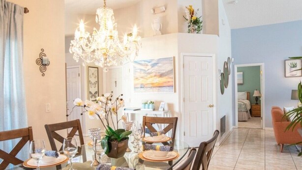 Un comedor con una mesa de vidrio, sillas y una araña. Hay una puerta que conduce a otra habitación.