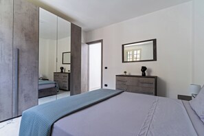 Ein modernes Schlafzimmer mit einem großen Bett, einer Kommode, einem Spiegel und einer Schiebetür zu einem anderen Raum.