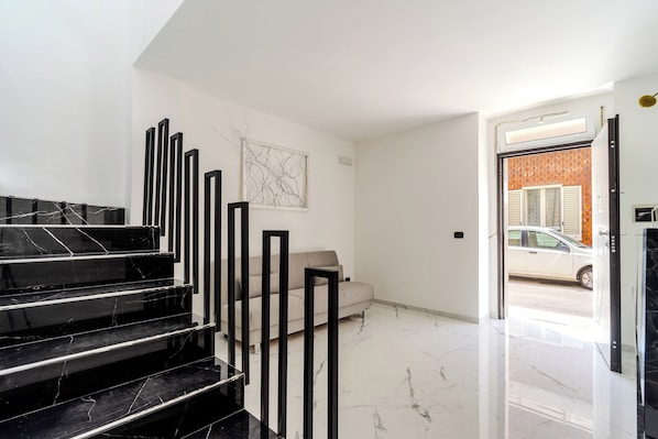 A modern interior with a marble staircase, a sofa, and a door leading outside.