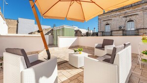 A rooftop patio with wicker furniture, a large umbrella, and a view of a historic building.