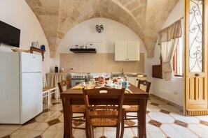 Une cuisine équipée d’une table à manger, de chaises, d’un réfrigérateur et d’un téléviseur fixé au mur.