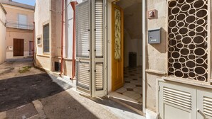 A narrow street with a building featuring a wooden door, a metal gate, and a decorative window grille.