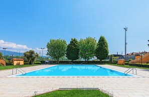 A rectangular swimming pool with a tiled deck, surrounded by trees and a fence. - I Girasoli D10 by Wonderful Italy (Toscolano Maderno)
