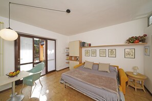 Una camera da letto con un letto, una scrivania, una sedia, un tavolino e uno scaffale con libri e fotografie.