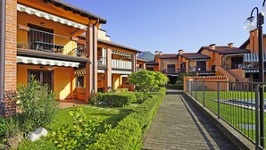 A row of brick buildings with balconies, a paved walkway, and a well-maintained garden. - I Girasoli D10 by Wonderful Italy (Toscolano Maderno)