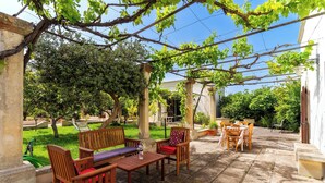 Une terrasse extérieure avec des meubles en bois, une pergola couverte de plantes grimpantes et un sol en pierre.