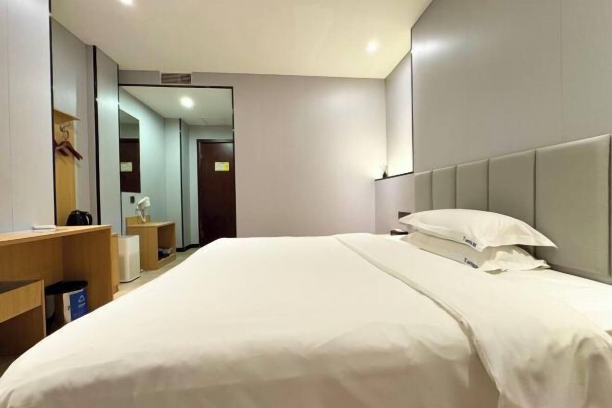 A modern hotel room with a large bed, a bedside table, a mirror, and a wardrobe.