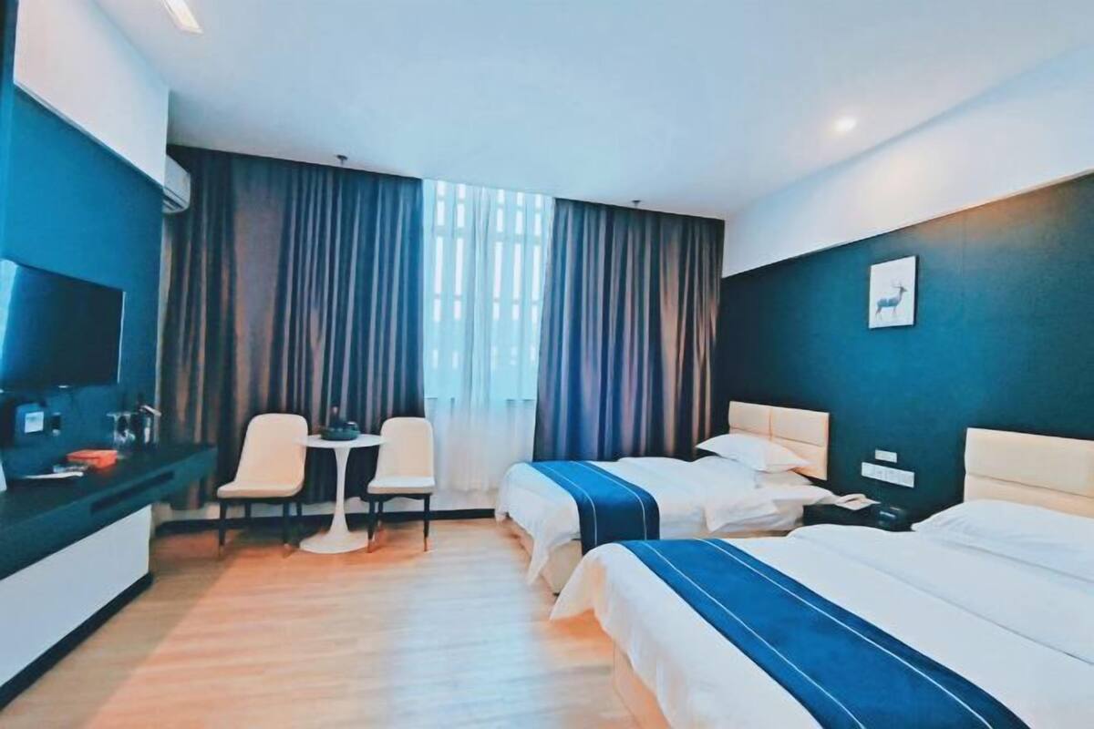 A hotel room with two beds, a desk, chairs, and a large window with curtains.