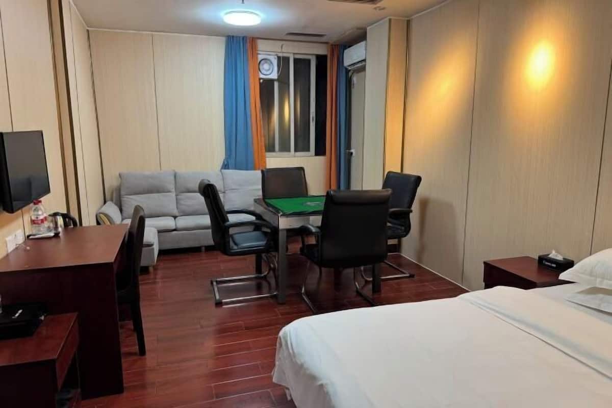 A hotel room with a bed, a desk, a sofa, and a gaming table.